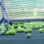 Many tennis balls next to the net on the court.