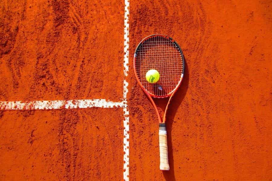 A tennis ball on a racket lying on a clay court.