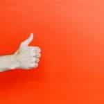 A hand with thumb up against orange backdrop.