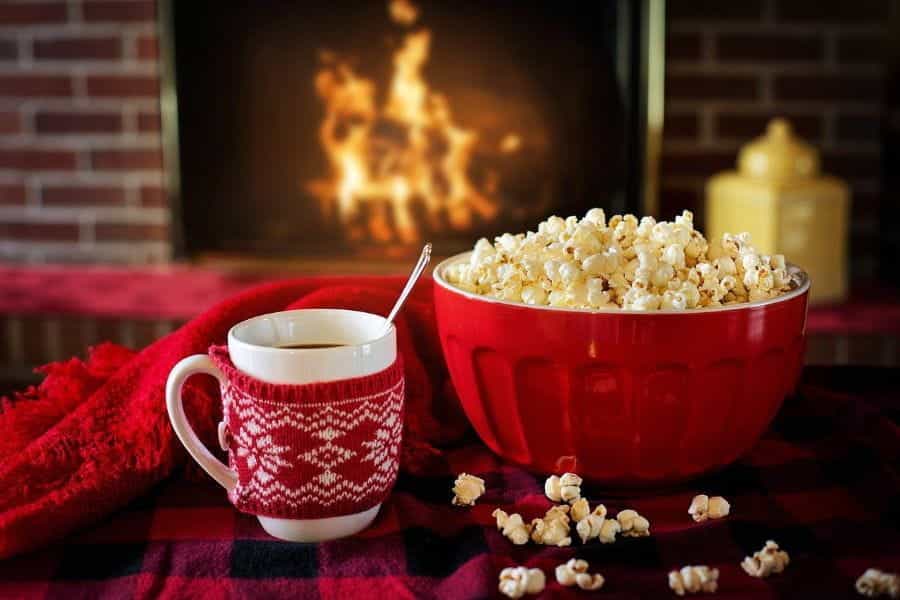 Secangkir cokelat panas dan semangkuk popcorn duduk di atas meja di depan api unggun.