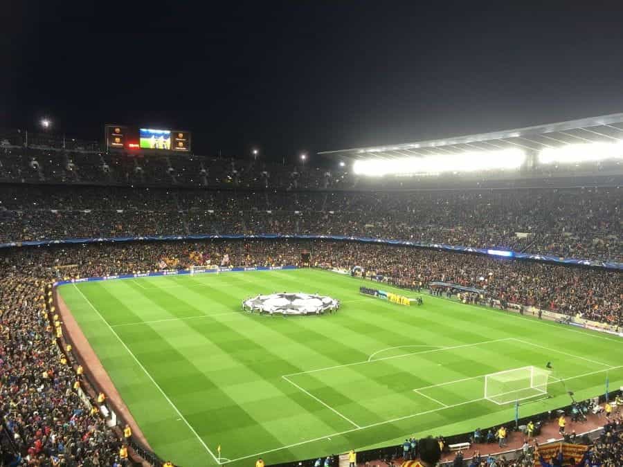 An illuminated football stadium at night, with a view of the pitch as both teams prepare for kickoff.