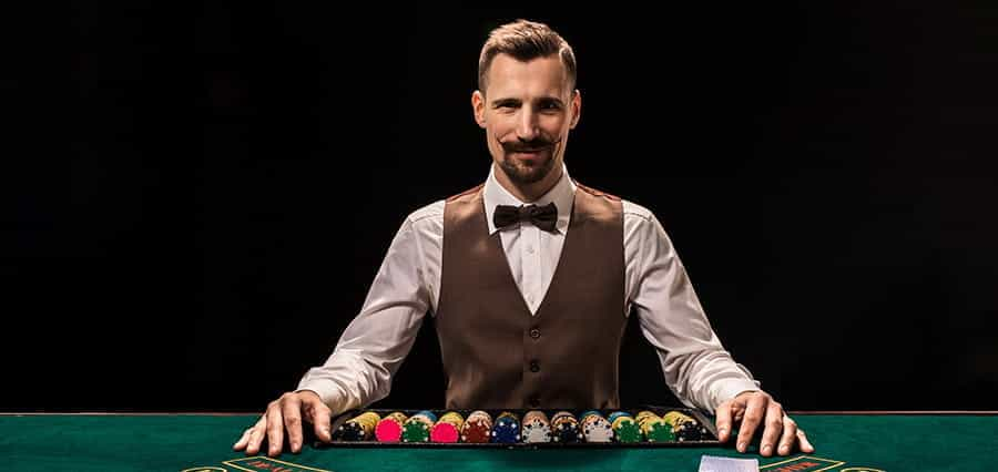 A croupier sitting at a table with casino chips and cards in front of him.