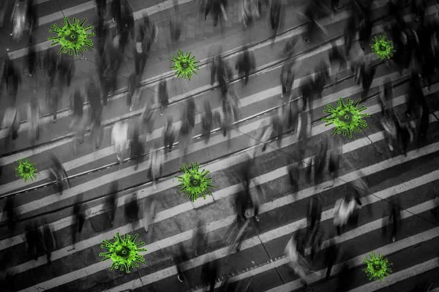 A crowd moves through a busy street superimposed with images of bright green coronavirus particles.