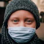 A child wearing a nose and mask covering during the coronavirus pandemic, staring into the camera.