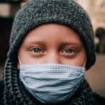 Seorang anak yang mengenakan penutup hidung dan masker selama pandemi virus corona, menatap ke kamera.