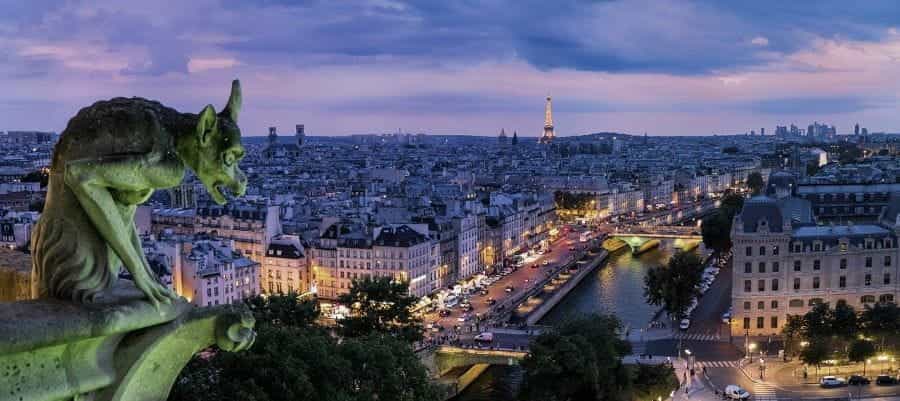 Gargoyle yang menghadap ke ibu kota Prancis, Paris pada malam hari, dengan Menara Eiffel yang ikonik terlihat di kejauhan.