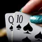 A hand with glittery nails holds some playing cards.
