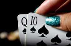 A hand with glittery nails holds some playing cards.