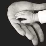 An adult’s hand holding a baby or infant’s hand.