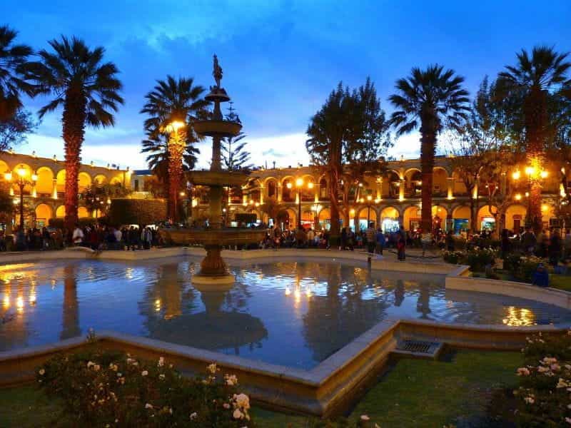 Dusk at a crowded outdoor plaza with a large water fountain in Arequipa, Peru.