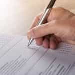 A person filling out a survey or report by checking boxes using a pen in their hand.