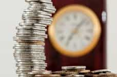 A stack of coins, with a clock in the background.