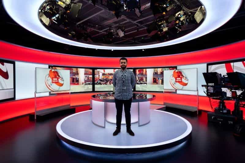 A man stands on the central stage of a BBC TV station, facing the cameras.
