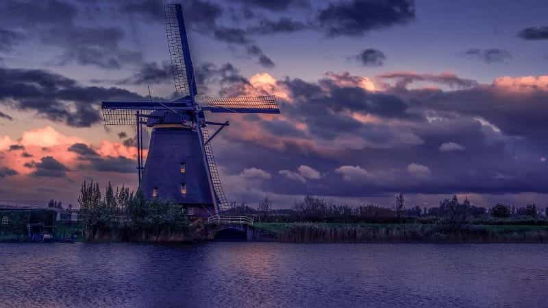 A typical Dutch windmill at the water’s edge, with a field stretching out behind it and off to its sides.