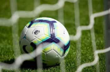 A soccer ball sitting on the pitch behind a goal, branded with the English Premier League’s logo.