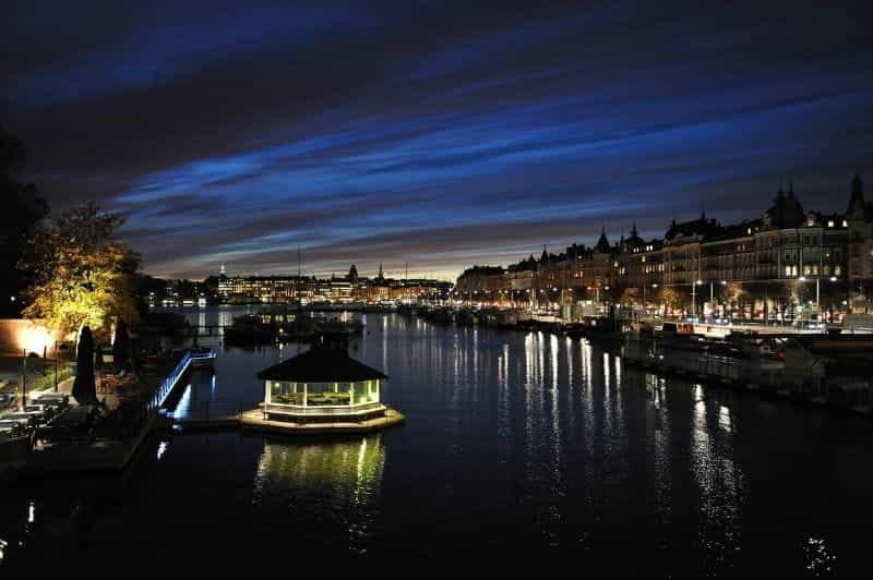 Sweden’s capital city of Stockholm during sunset, with a river channel surrounded by lights and docks in center view.