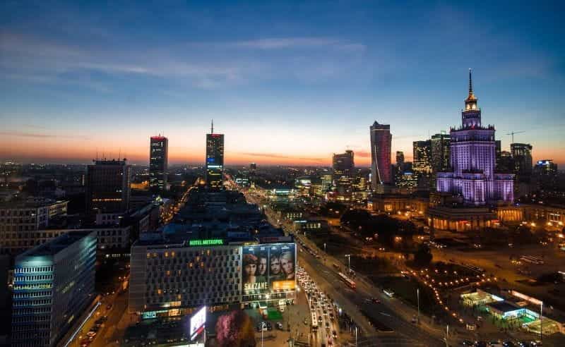The Polish capital city of Warsaw’s nighttime skyline, featuring prominent skyscrapers and large boulevards.