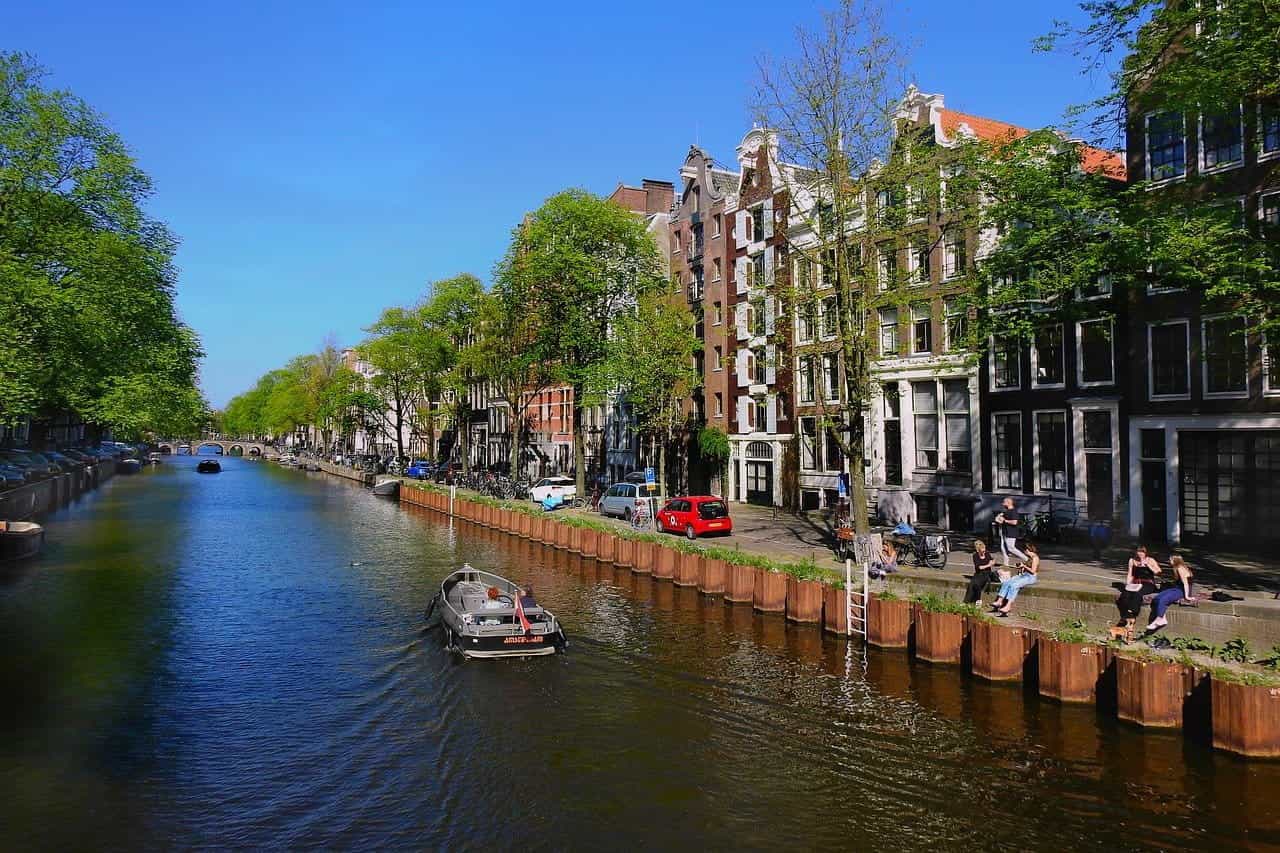 One of the Dutch capital city Amsterdam’s numerous canals on a bright sunny day, with a small boat sailing down the canal.