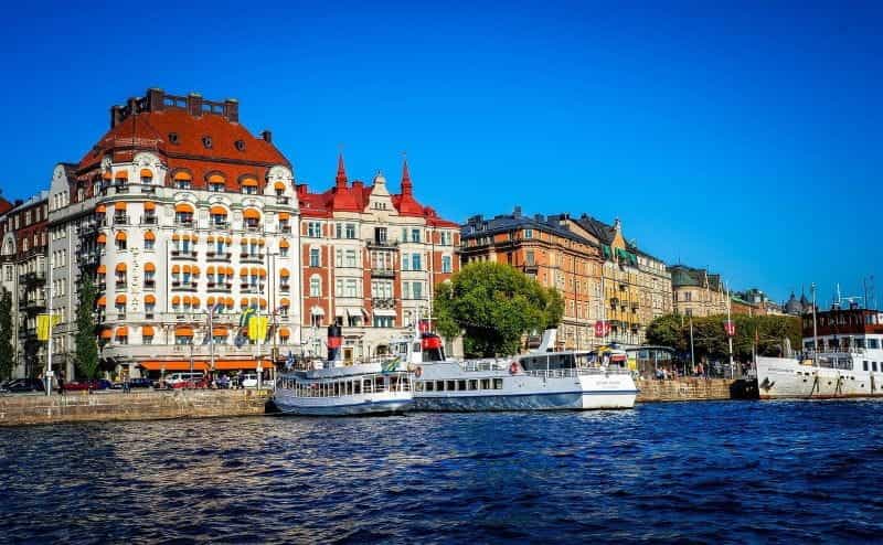 The waterfront of Sweden’s capital city of Stockholm on a clear, sunny day, with several ferry boats in the center.
