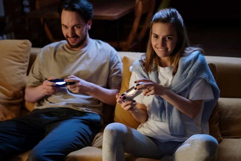 Sepasang kekasih bermain video game bersama di atas sofa.