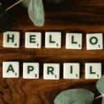 Scrabble letter tiles that say HELLO APRIL, with leaves and plants.