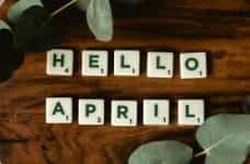 Scrabble letter tiles that say HELLO APRIL, with leaves and plants.