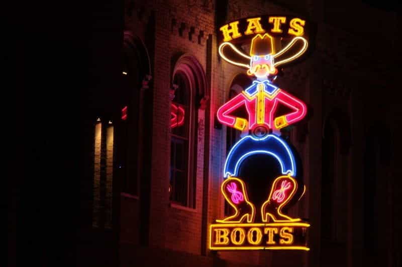 A neon sign depicting a cowboy with the word HATS over his head and the word BOOTS under his boots.