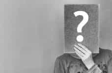 A person holding a rectangular form in front of their face with a large question mark on it.