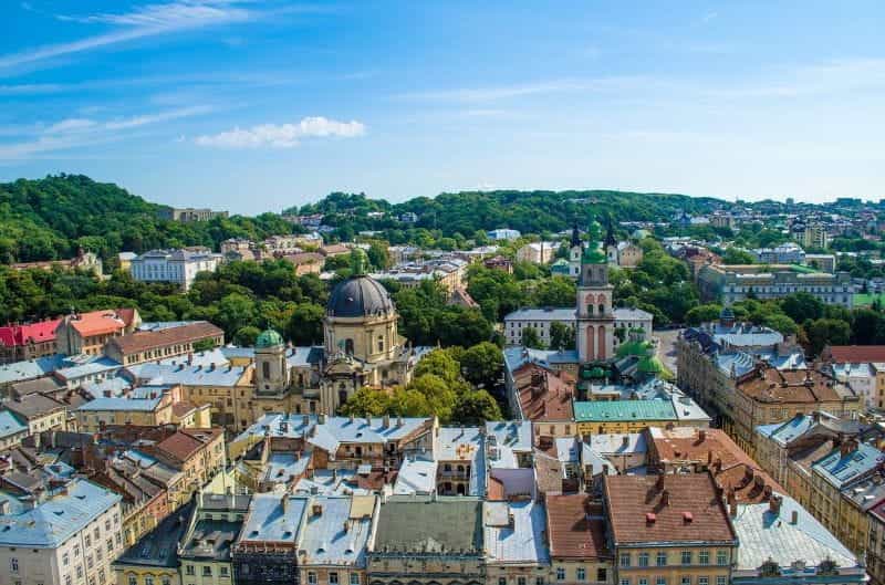 The Ukrainian city of Lviv in the summertime, with churches and buildings dotting the green, hilly landscape.
