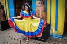 A woman wearing traditional Colombian dress holds out her skirt and smiles.