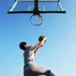 A person going for a lay-up while playing basketball on a clear blue sky day.