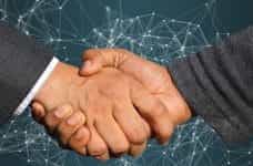 Two hands in suits shaking in front of a digital background.