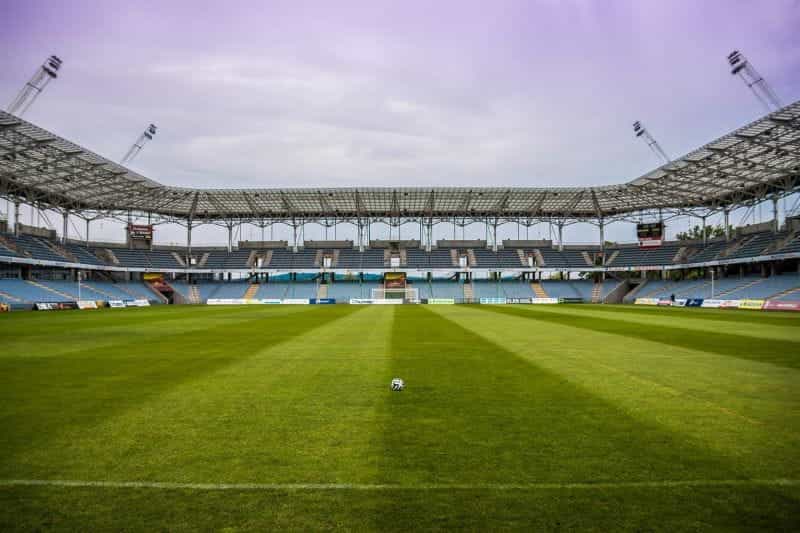 A football in the middle of a pitch in an empty stadium.