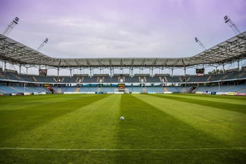 An empty football pitch in a football stadium, with one lone football sitting alone on the grass.