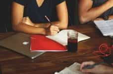 A person sitting at a table during a meeting in front of a closed laptop and paperwork.