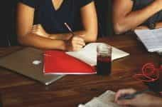 A person sitting at a table during a meeting in front of a closed laptop and paperwork.