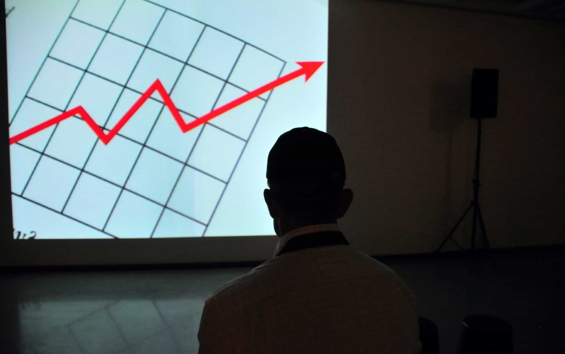 A man looks at a chart which shows a red arrow trending upward.