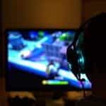 The silhouette of the back of a person while they play a videogame with a headset on.