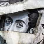 Torn up banknotes reveal part of a face printed on the money, looking at the viewer.