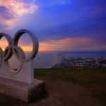 Olympic rings statue overlooking the sea and a city.