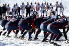 Alt Text: A row of football players in the snow getting ready for a play.
