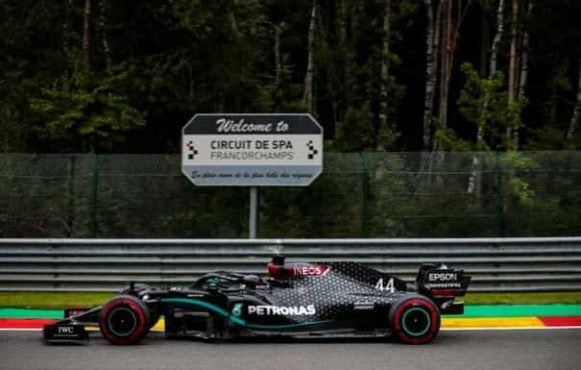 A Mercedes F1 car passes a Circuit De Spa road-sign at high speed.
