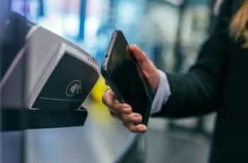 A hand holds a smartphone up to a contactless payment point.