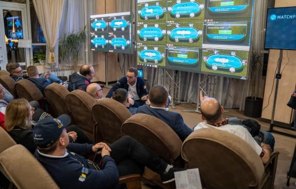 Spectators watching a bank of screens displaying animated poker tables.