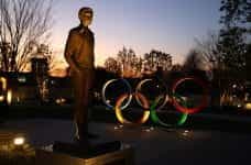Sun sets on a bronze statue Baron de Coubertin alongside the famous Olympic rings.