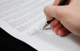 A hand signing a legal document with a pen.