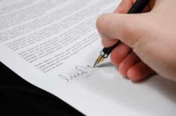 A hand signing a legal document with a pen.