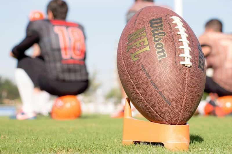 An American football perched on a stand ready to be kicked.