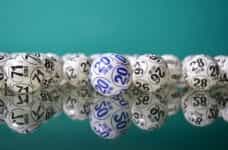 White lottery balls marked with grey and blue text sit on a mirrored surface.