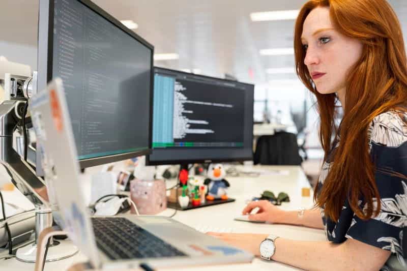 A woman working on a computer at a desk, with extra monitors.